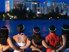 A group of friends enjoys a vibrant night by the water, adorned with glowing accessories, creating a festive atmosphere perfect for celebrations.
