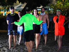 A lively group participates in a beach party activity at night, showcasing vibrant glow accessories and a fun atmosphere perfect for memorable celebrations.