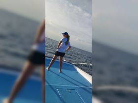 A woman stands confidently on the deck of a boat, enjoying the ocean breeze under a clear sky — a perfect moment for adventure on the water.