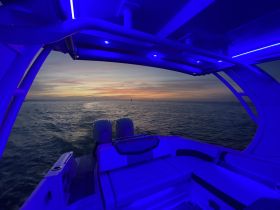 A serene view from inside a boat's cabin, showcasing comfortable seating and a stunning sunset over the water — perfect for evening cruises.