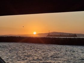 A stunning sunset view framed by the edge of a boat, showcasing a distant island and tranquil waters — perfect for capturing the beauty of evening cruises.