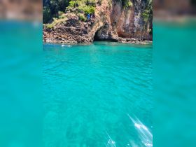 A group of people enjoys a sunny day by the rocky coastline, with one person swimming in the vibrant turquoise waters — a perfect spot for adventure and exploration.