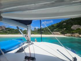 A picturesque view from a sailboat, showcasing a serene beach and lush greenery, with a person enjoying the stunning tropical scenery.