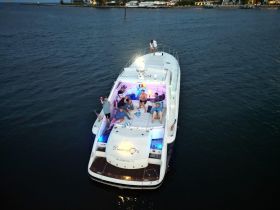 A lively group enjoys a fun evening aboard a yacht, celebrating with drinks and laughter under colorful lights — perfect for memorable gatherings on the water.