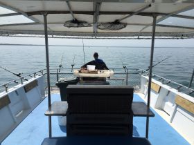A view from the interior of a fishing boat, showcasing the helm area with fishing rods set up and a person preparing for a day on the water.