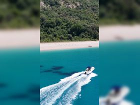 An aerial view of a speedboat cruising through crystal-clear turquoise waters, showcasing the stunning beach and lush greenery in the background.