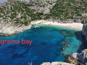 A stunning aerial view of Grama Bay, showcasing its pristine beach and turquoise waters, with visitors enjoying the sun and sand — a perfect destination for relaxation and exploration.