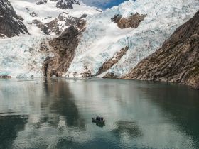 A small boat navigates the serene waters near a stunning glacier, reflecting the majestic landscape of Alaska — a perfect adventure for nature lovers.