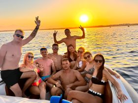 A lively group of friends celebrates at sunset aboard a boat, capturing the essence of summer fun and camaraderie on the water.