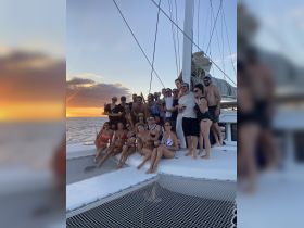 A lively group celebrates aboard a catamaran at sunset, capturing the essence of fun and camaraderie on the water.