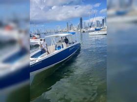 Two men aboard the 'Malambo' boat in a bustling marina, with a stunning city skyline in the background — a perfect setting for exploring coastal waters.
