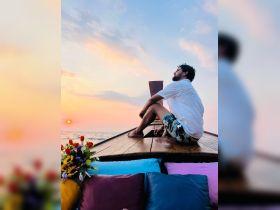 A man enjoys a serene sunset view from the bow of a boat, surrounded by colorful cushions and flowers — a perfect moment for relaxation on the water.