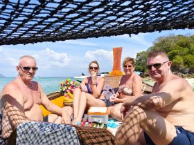 A cheerful group enjoys a sunny day on a boat, surrounded by clear waters and beach scenery — perfect for a fun-filled day of snorkeling and relaxation.