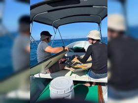 Two individuals prepare a surfboard on a boat in the ocean, showcasing a fun day of water activities.