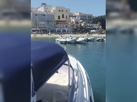 A picturesque view of a yacht docked near a beach, with charming buildings in the background, perfect for a relaxing day on the water.