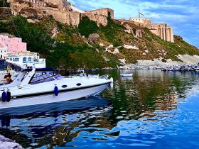 A sleek speedboat docked in a serene harbor, reflecting the stunning architecture of the cliffs above — a picturesque scene perfect for boating enthusiasts.