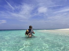 A father and his two children enjoy a fun day swimming in the crystal-clear waters of a tropical beach, creating unforgettable family memories.