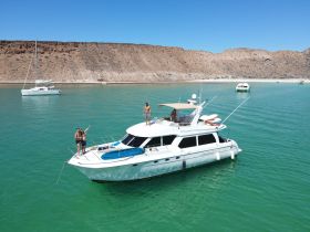 A lively group enjoys a sunny day aboard a yacht, with one person standing on the bow and others celebrating in the water — a perfect scene for summer fun and beach adventures.
