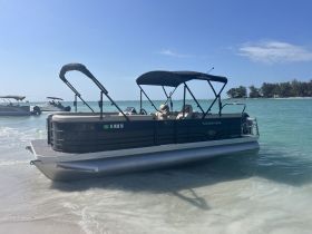 A sleek pontoon boat is docked on a sandy beach, showcasing its spacious design and inviting seating — perfect for leisurely days on the water.