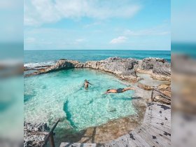 A couple enjoys a refreshing swim in a stunning natural pool by the ocean, surrounded by rocky formations and crystal-clear waters — an idyllic beach getaway.
