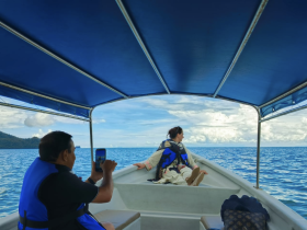 A serene moment on a boat with a woman enjoying the view of the ocean while a companion captures the experience on their phone — perfect for adventure seekers and ocean lovers.