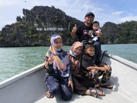 A cheerful family poses for a photo on a boat near Kilim Geoforest Park, showcasing their adventure with thumbs up and smiles against a stunning natural backdrop.