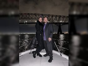 A couple poses for a romantic photo on a boat at night, with a stunning bridge illuminated in the background — perfect for memorable celebrations on the water.
