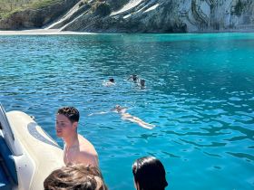 A group enjoys a refreshing swim in crystal-clear waters, surrounded by stunning coastal scenery — perfect for a day of fun and relaxation on the water.