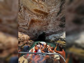 A lively group enjoys a boat tour exploring stunning rock formations and caves, capturing the moment with their cameras in a picturesque setting.