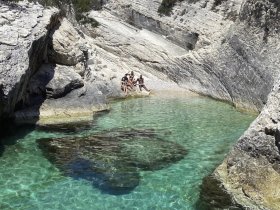 A group of friends relaxes by the crystal-clear waters of a secluded cove, enjoying the stunning natural scenery — perfect for a day of swimming and sunbathing.