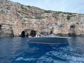 A sleek boat navigates the stunning coastline, showcasing dramatic cliffs and clear waters — perfect for an adventurous day on the water.