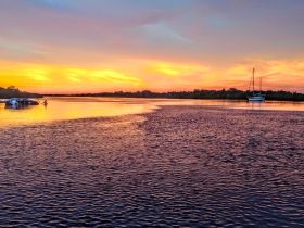 A stunning sunset over a tranquil waterway, featuring a sailboat anchored in the distance — a perfect scene for nature lovers and boating enthusiasts.