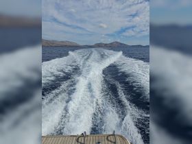A stunning view from the back of a boat, showcasing the wake as it cuts through the water, with picturesque mountains in the background — perfect for showcasing the beauty of a boating adventure.