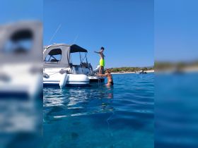 A young boy stands on the edge of a boat while a woman prepares to join him in the crystal-clear water, capturing a joyful summer moment on the water.