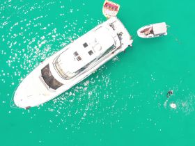 A stunning aerial view of a yacht anchored in vibrant turquoise waters, with guests enjoying a swim nearby — perfect for showcasing luxury boating experiences.