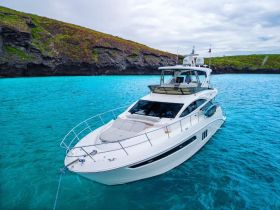 A stunning aerial view of a luxurious yacht anchored in crystal-clear turquoise waters, surrounded by lush rocky cliffs — perfect for exploring beautiful coastal destinations.