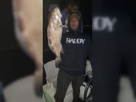 A proud angler displays a large catch during a night fishing trip, showcasing the thrill of fishing adventures on the water.