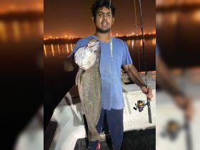 A young adult proudly displays a large catch while fishing at night, showcasing the thrill of nighttime fishing adventures.