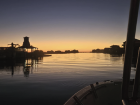 A serene sunset view from a boat, showcasing a tranquil waterway and silhouetted structures along the shore — perfect for peaceful evening cruises.