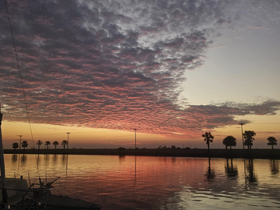 A stunning sunset reflects on calm waters, framed by palm trees, creating a picturesque scene perfect for evening boat outings.