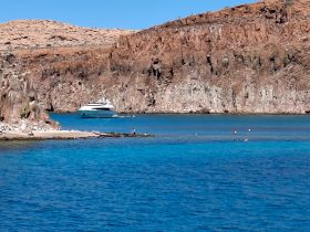 A stunning view of a yacht anchored near a beach, with swimmers enjoying the clear turquoise waters — a perfect destination for relaxation and adventure.