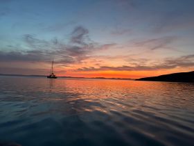 A serene sunset view featuring a sailboat gliding across calm waters, creating a picturesque scene perfect for tranquil evening cruises.