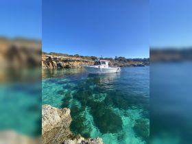 A picturesque view of a boat anchored in crystal-clear waters, surrounded by stunning rocky cliffs — an ideal setting for a tranquil day on the water.