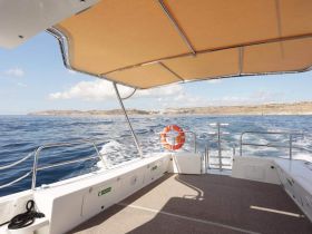 A spacious interior view of a boat's helm area, featuring a shaded seating space and a scenic backdrop of the coastline, perfect for relaxing while cruising.