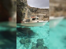 A stunning view of a boat anchored in crystal-clear waters, surrounded by dramatic cliffs — perfect for exploring Malta's beautiful coastline.