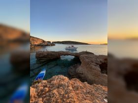 A serene sunset view featuring a boat anchored near rocky formations, perfect for capturing the beauty of coastal adventures.