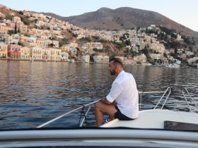 A man enjoys the serene view from the bow of a boat, overlooking a picturesque coastline with colorful houses — a perfect moment for relaxation and exploration.