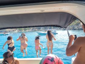 A group of friends joyfully jumps into the crystal-clear waters from their boat, capturing the essence of summer fun and adventure on the water.