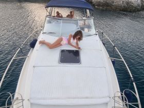 A woman relaxes on the deck of a boat while two others enjoy the view in the background — a perfect moment of leisure on the water.