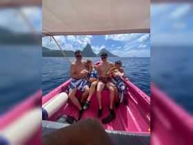 A cheerful family enjoys snacks aboard a vibrant pink boat with stunning mountain scenery in the background, perfect for a memorable day on the water.